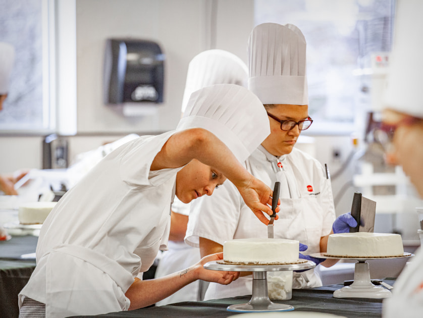 A student in a chef's hat frosts a cake.