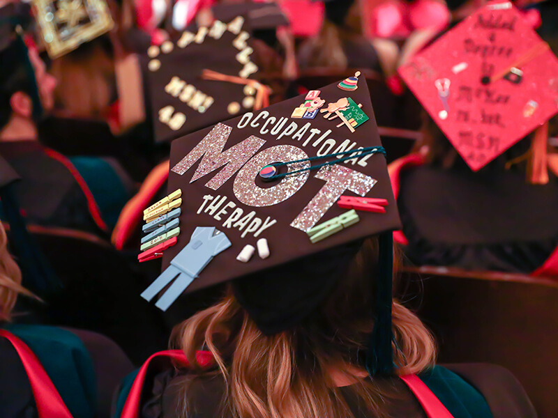 A graduation cap decorated with ribbons and clothespins and glittery text as seen from above