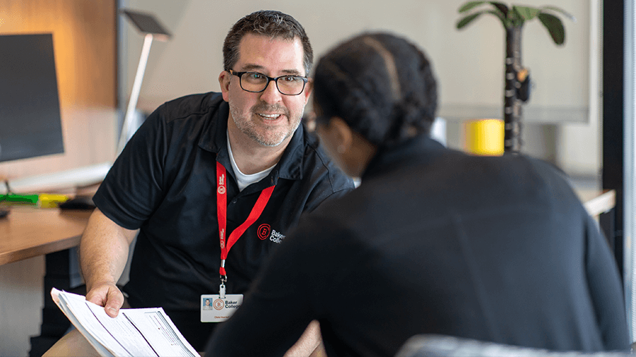 An advisor wearing a red Baker lanyard speaks with a student.