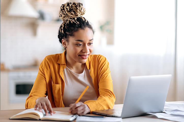 A student looking at a laptop and taking notes.